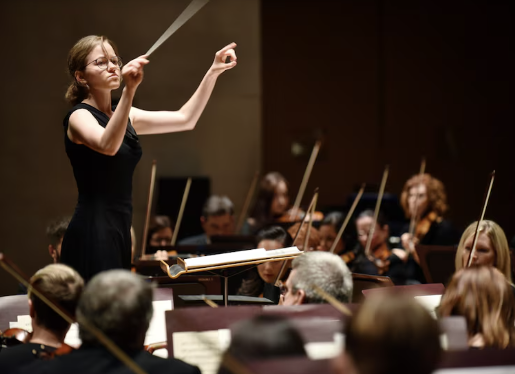 A conductor leads an orchestra, emphasizing teamwork and synchronization among musicians in a performance setting.